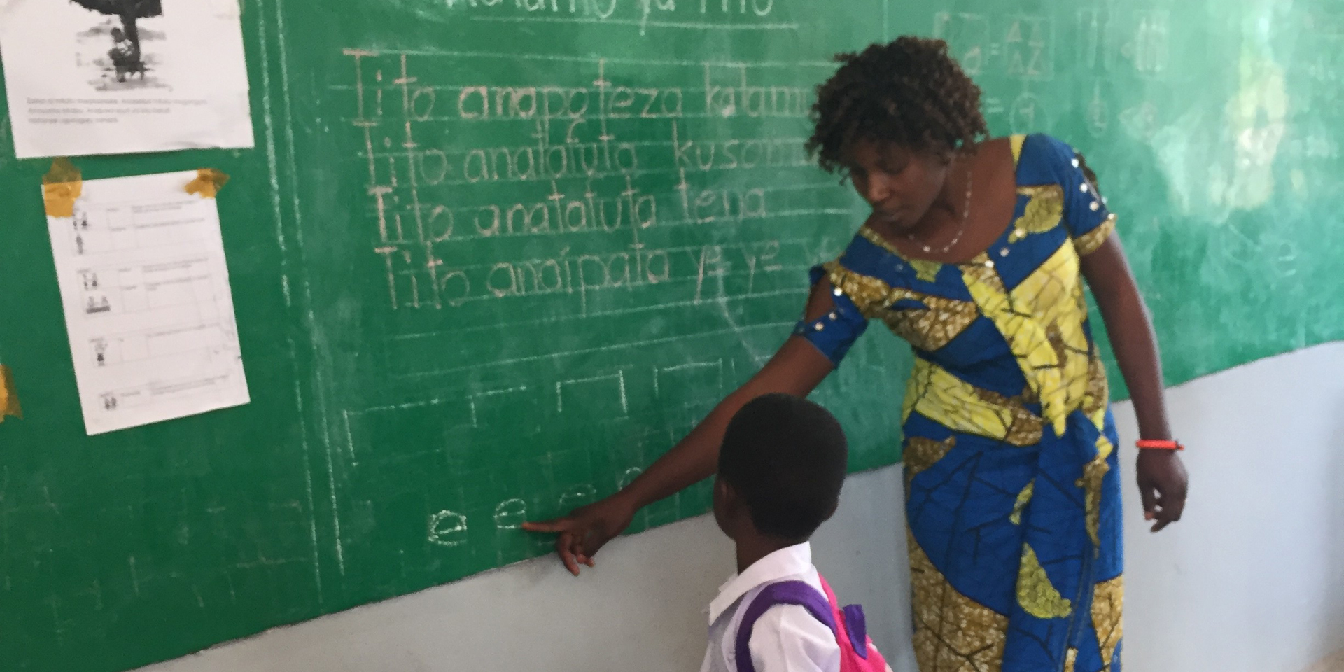 Image of a teacher pointing out a letter on a blackboard to a young student beside her.