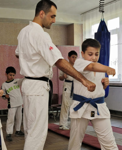 Several boys in a gym receiving martial arts instruction from a teacher.