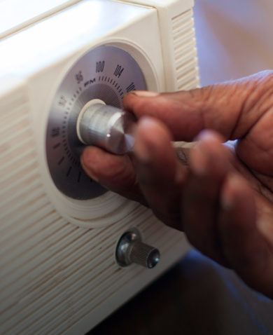 A close-up image of a hand moving the dial of a radio.