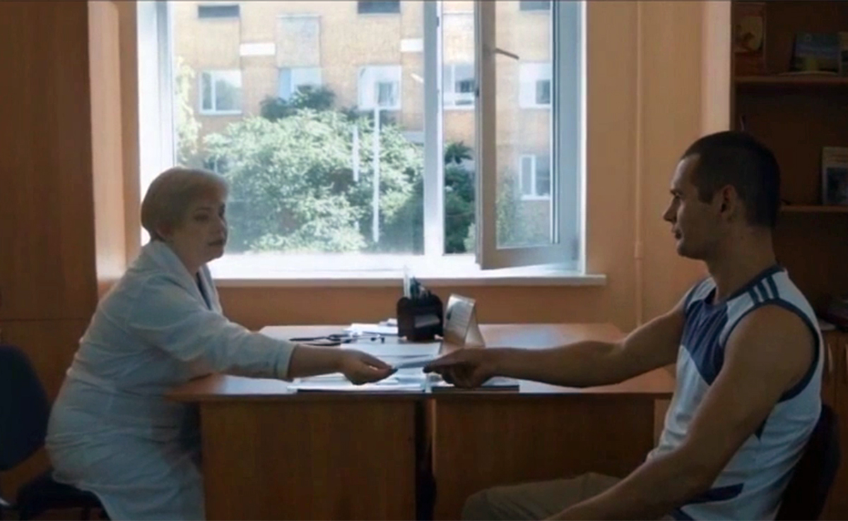 Image of two people sitting across from one another at a desk. One gives a pamphlet to the other.