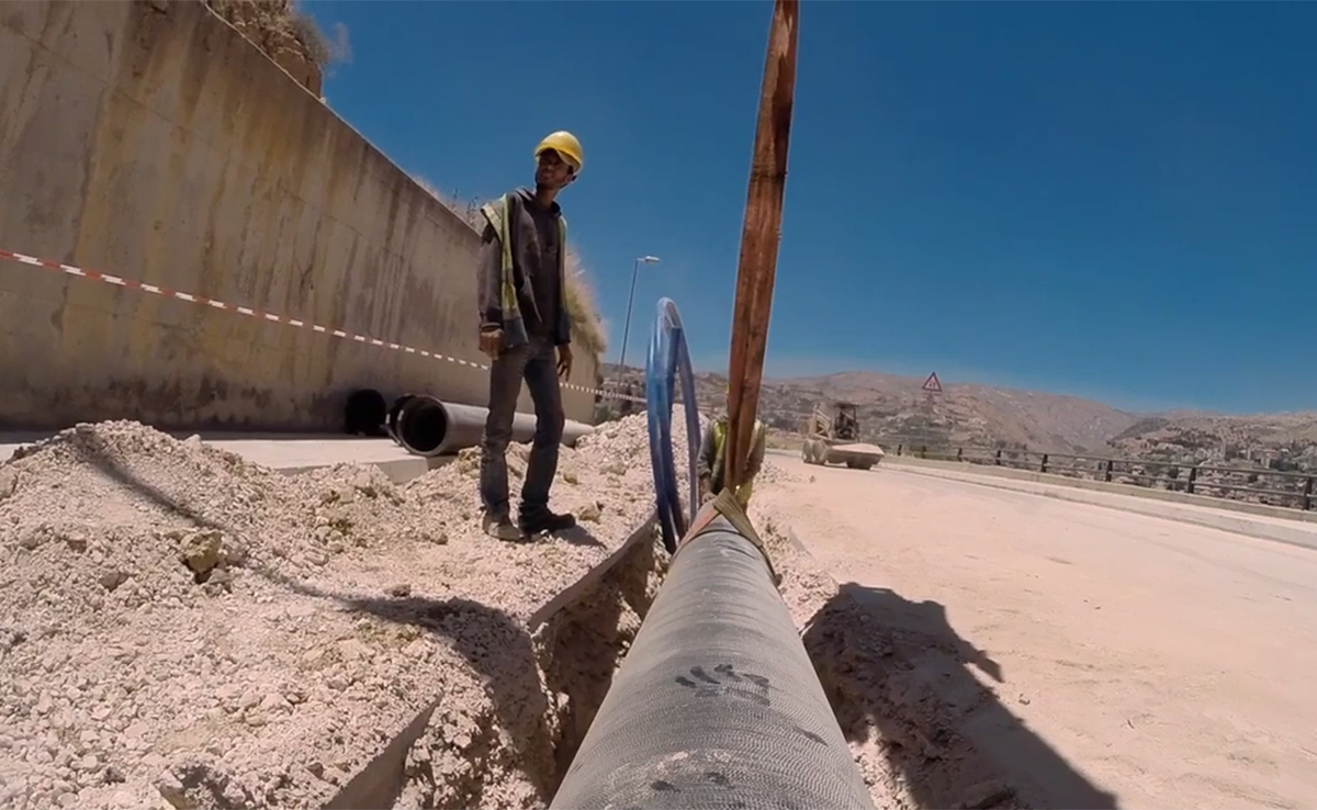 Image of a large pipe being laid into the ground as a construction worker stands beside it.