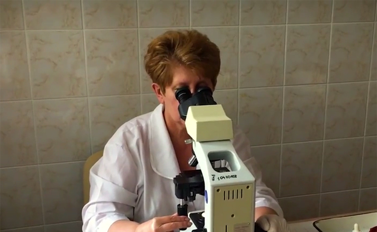A woman in a white lab coat looking into a microscope.