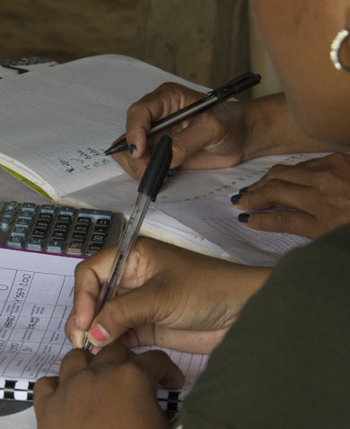 Image of two people sitting at a table and writing into workbooks with a calculator between them.