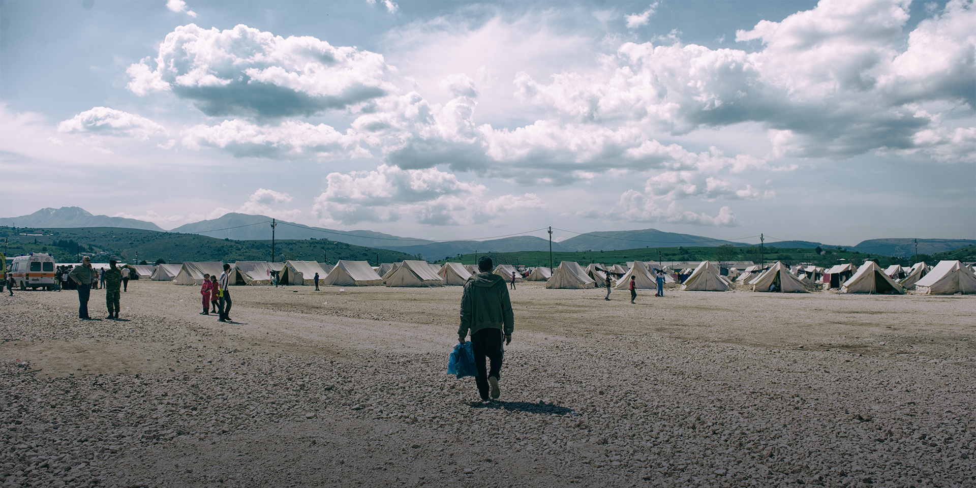 A man walking toward a large group of white tents in the background.