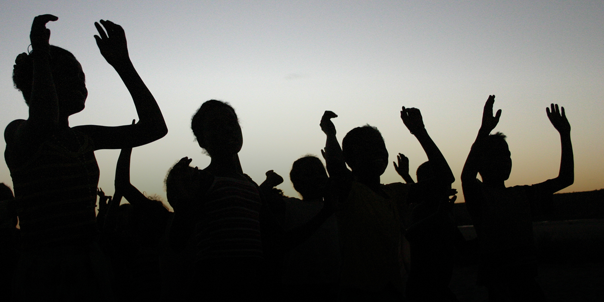 Image of several young people waving their arms as the sun sets.