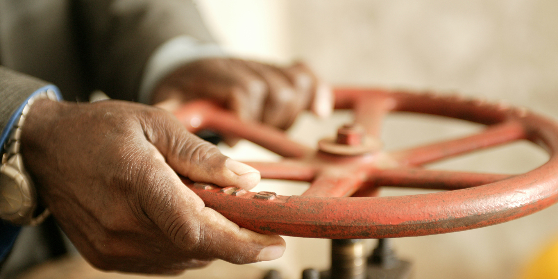 A close-up of hands turning a large, red valve.