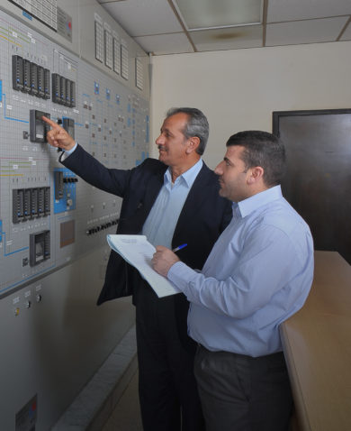 Two men examine a control panel in Jordan.
