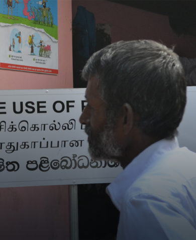 A man looking at a poster showing a cartoon of a person reaching for pesticide next to a sack of grain. A sign the man reads "Safe Use of Pesticides."