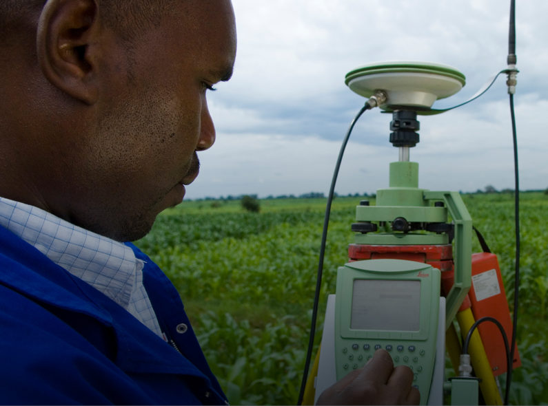 A man surveying farmland with a large green device with a keypad he is using to input figures.