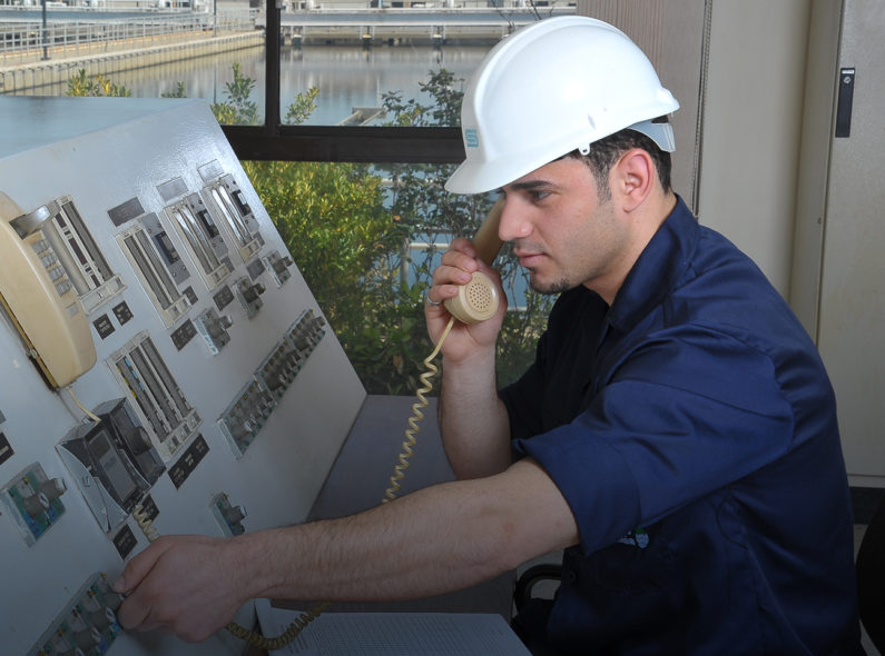 Image of a man in a hard hat operating a switchboard.