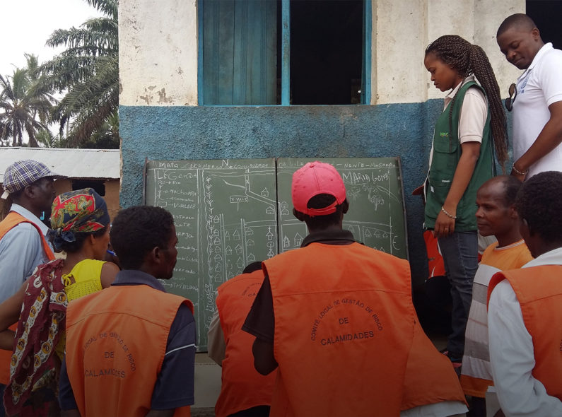 A group of people in orange vests outside reviewing a blueprint drawn on a blackboard.