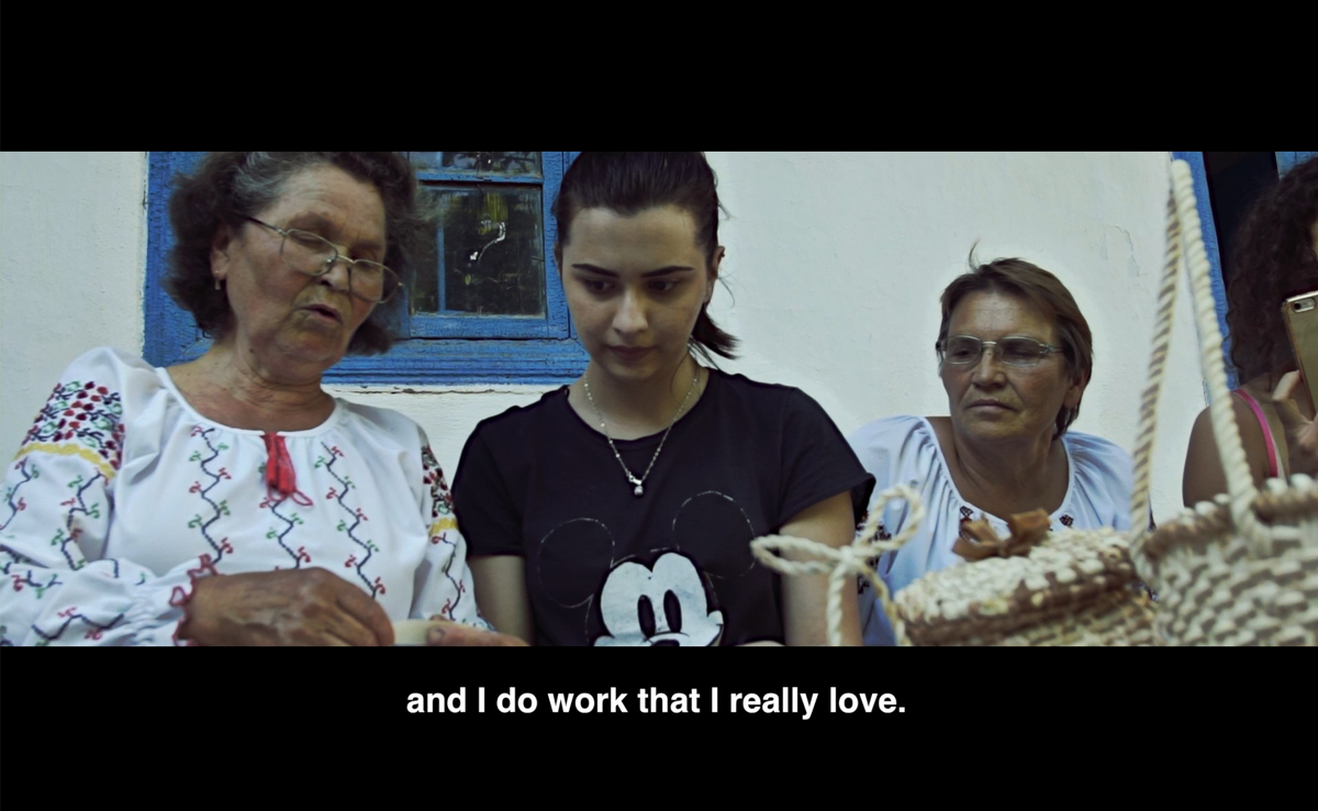 Image of an older woman showing crafts to a younger woman. Below the image is a closed caption that reads "and I do work that I really love."