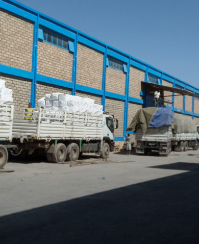 The outside of a warehouse with several white trucks loading and unloading goods.