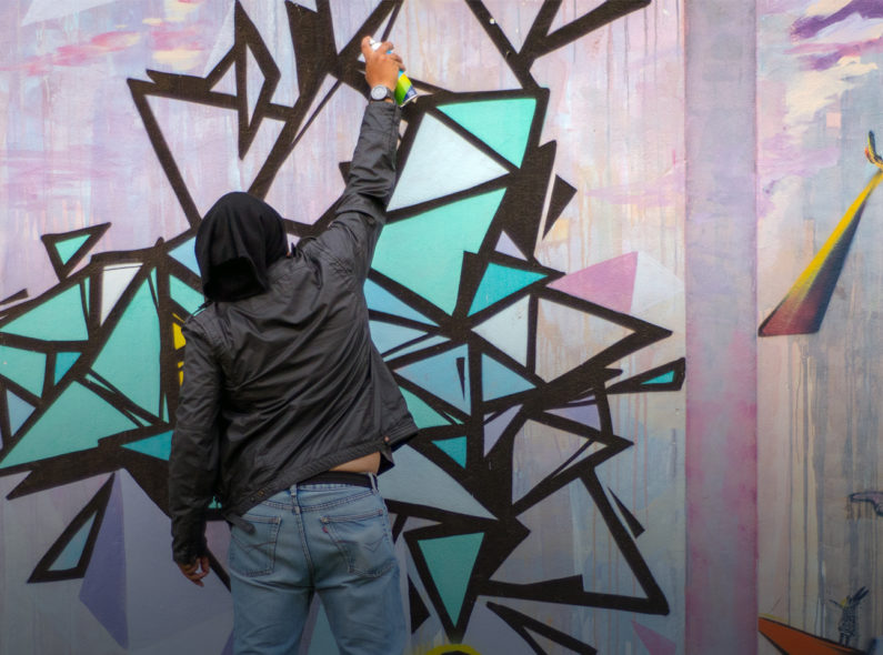 A person spray painting a mural on a wall.