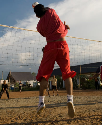 Image of several people playing volleyball as a small child sits and watches from the sidelines.