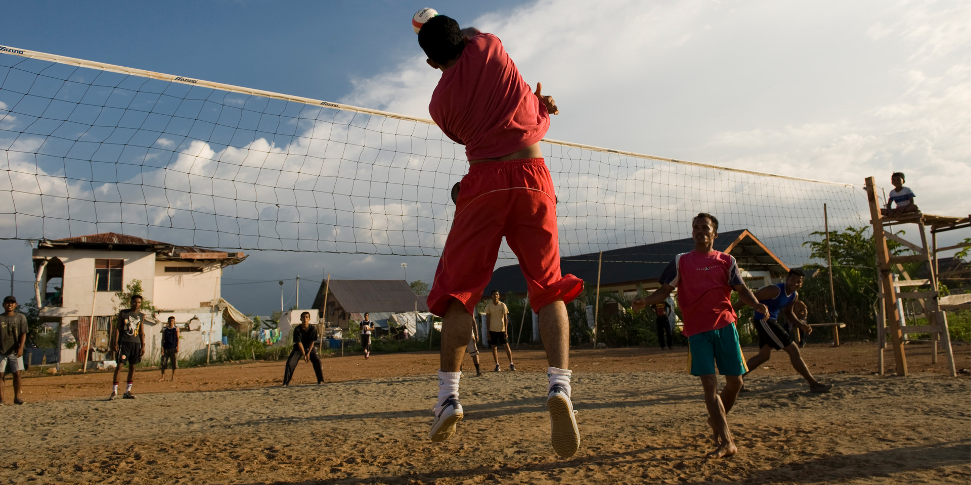 Image of several people playing volleyball as a small child sits and watches from the sidelines.