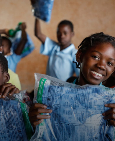 A group of children smiling and holding blankets wrapped in plastic packaging.