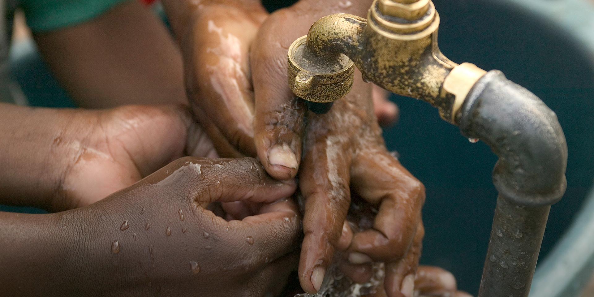 A close-up image of several people washing their hands under a waterspout.