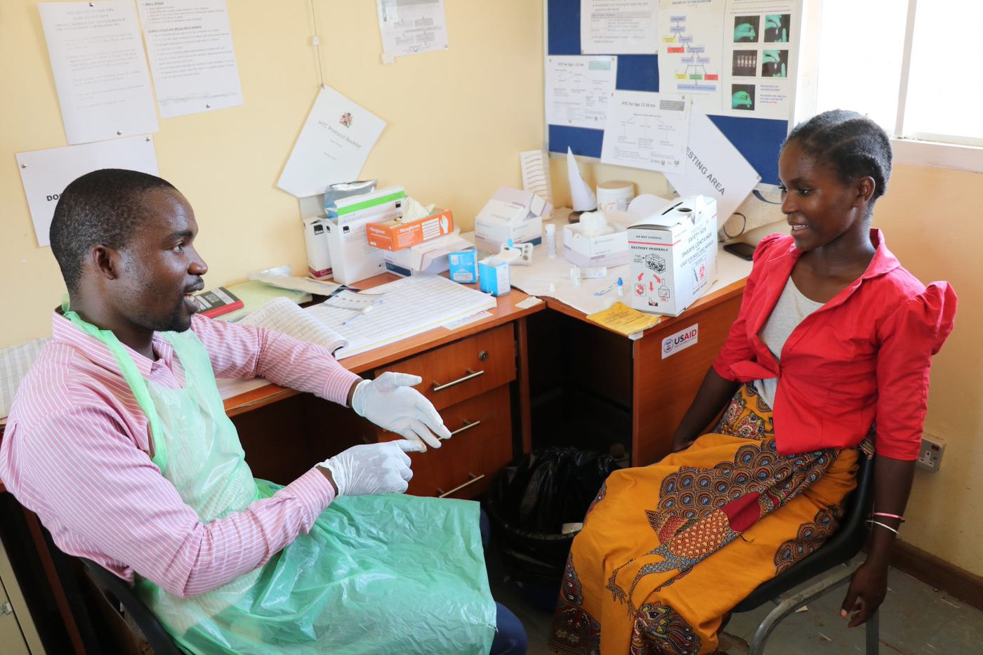 A healthcare worker sitting at a desk and having a discussion with a smiling woman.