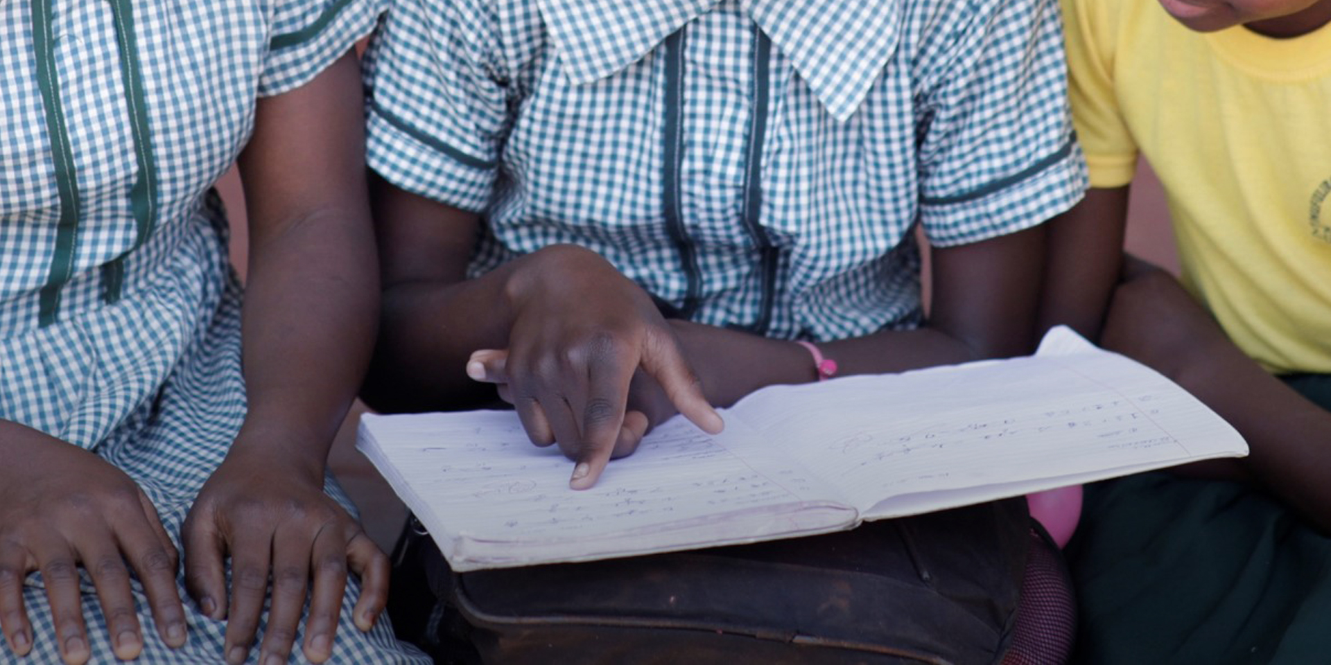 A close-up image of three children reading a notebook together.