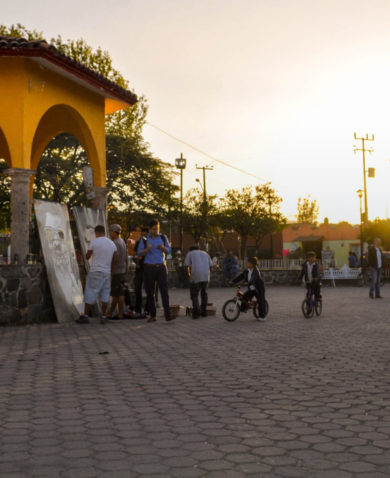 Image of a paved city center with several people painting large portraits that are leaning against a gazebo.