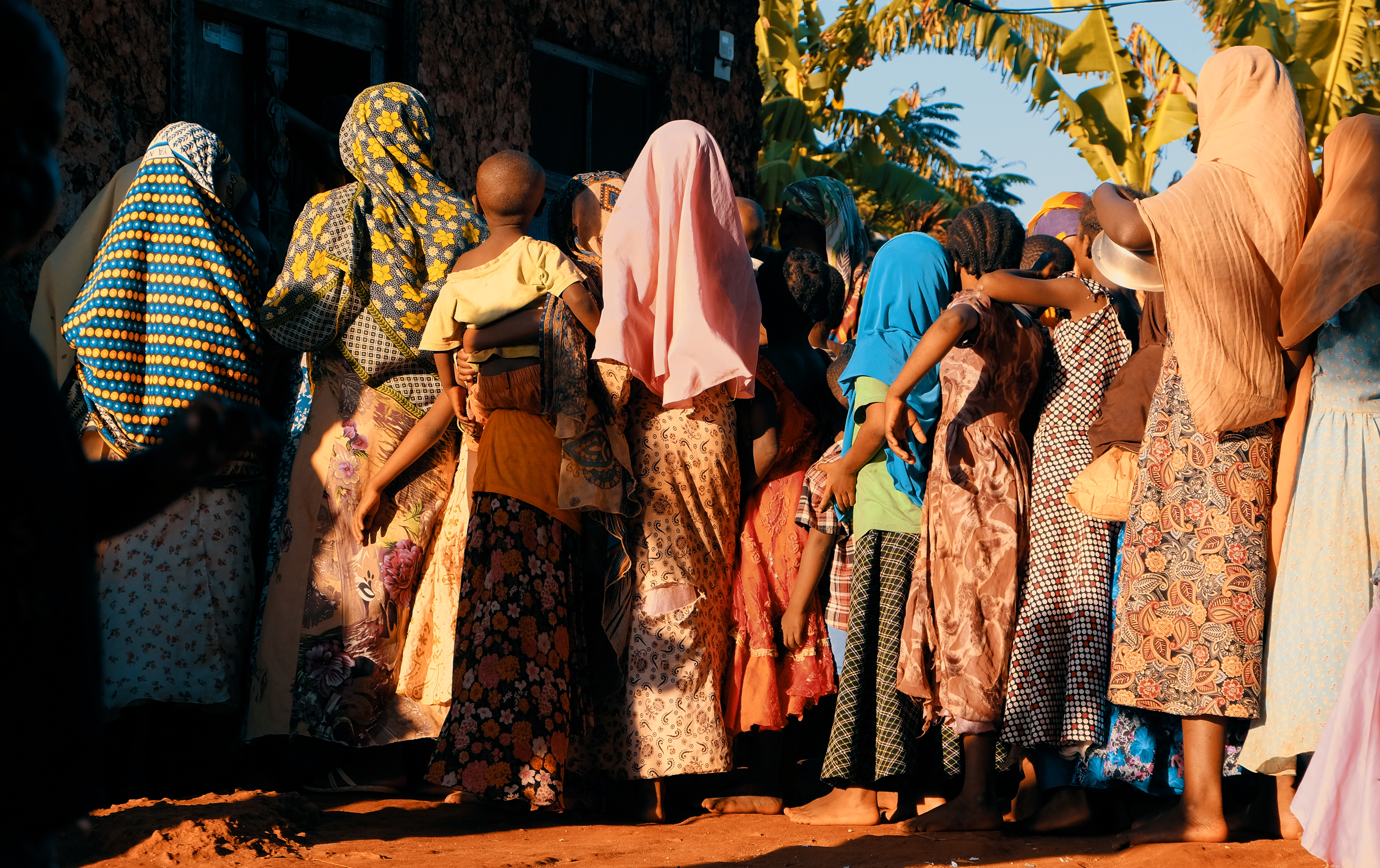 Image of several women and children standing in line outside a building.