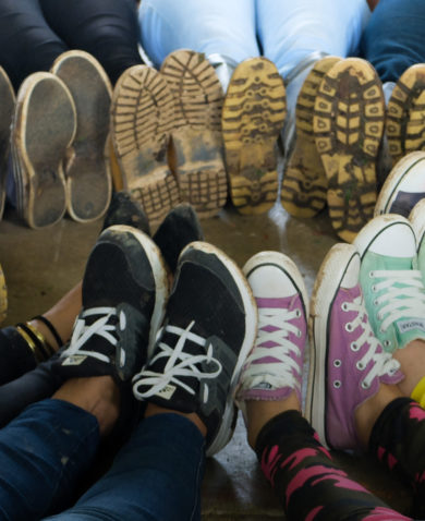 Image of several people putting their shoed feet together in the shape of a circle.