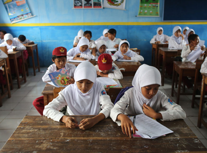 A classroom filled with schoolchildren sitting at school desks.