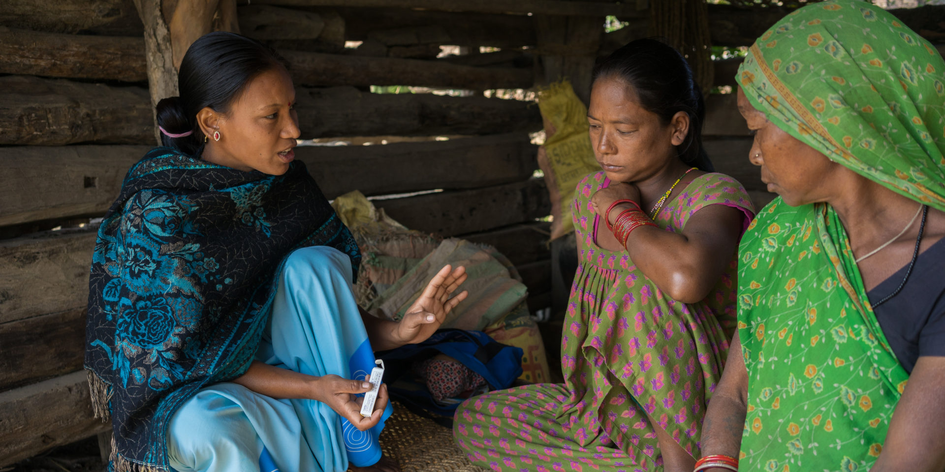 A community health volunteer speaking with a pregnant woman in her home as another woman listens.