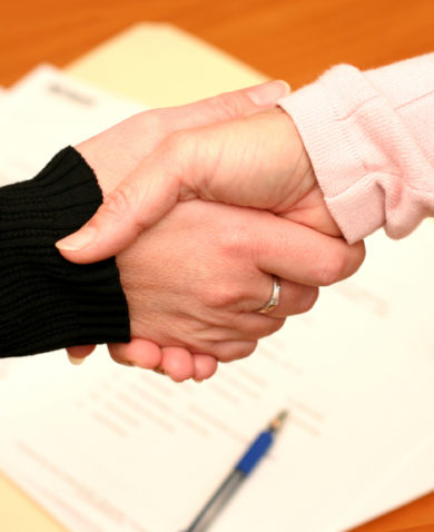 A close-up of a handshake above a manilla folder with signed documents.