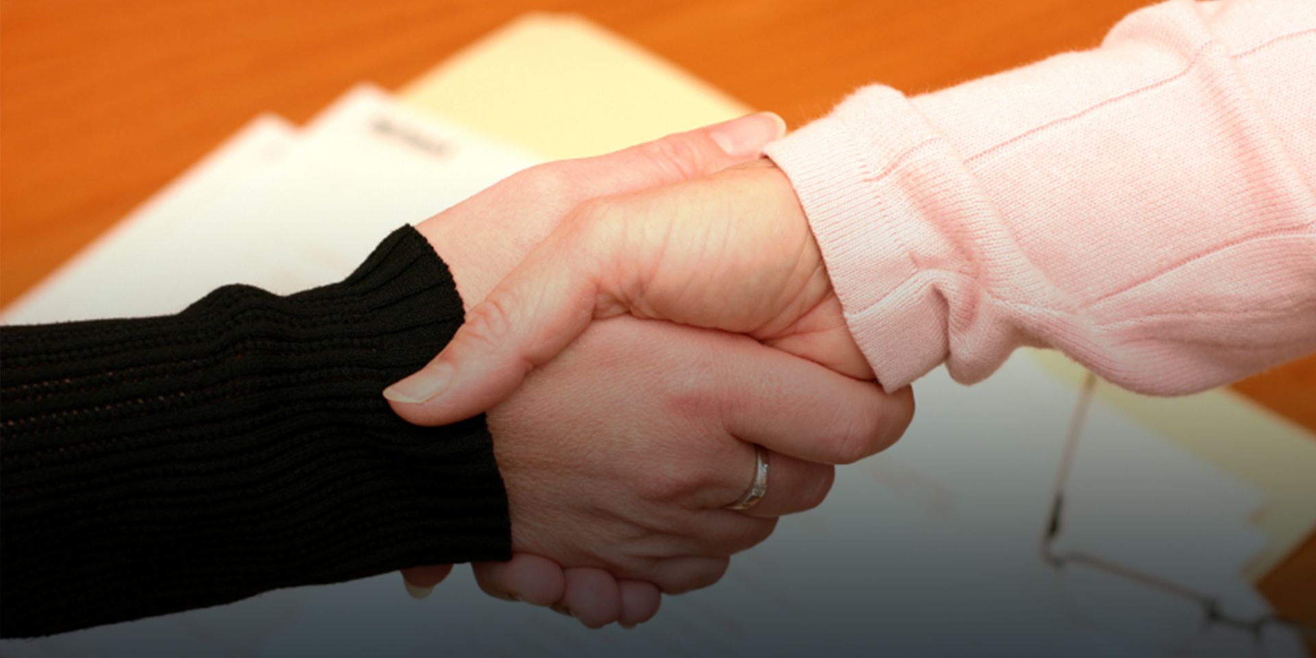 A close-up of a handshake above a manilla folder with signed documents.