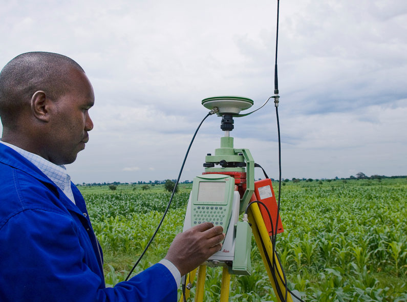 A man standing in farmland and using a keypad on a satellite device on a tripod.