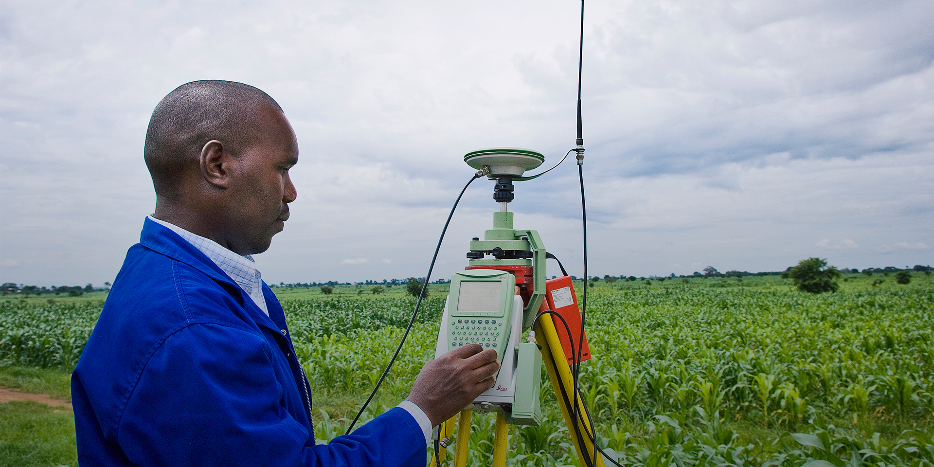 A man standing in farmland and using a keypad on a satellite device on a tripod.