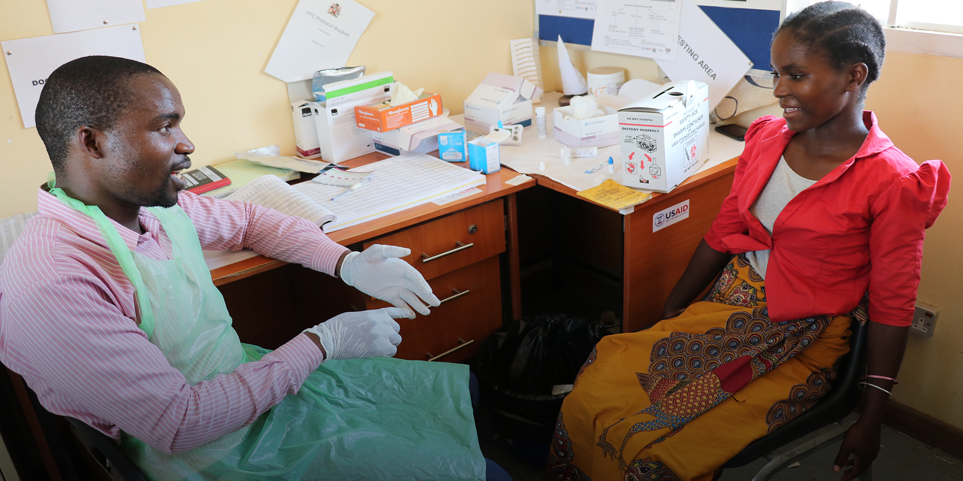 A healthcare worker sitting at a desk and having a discussion with a smiling woman.