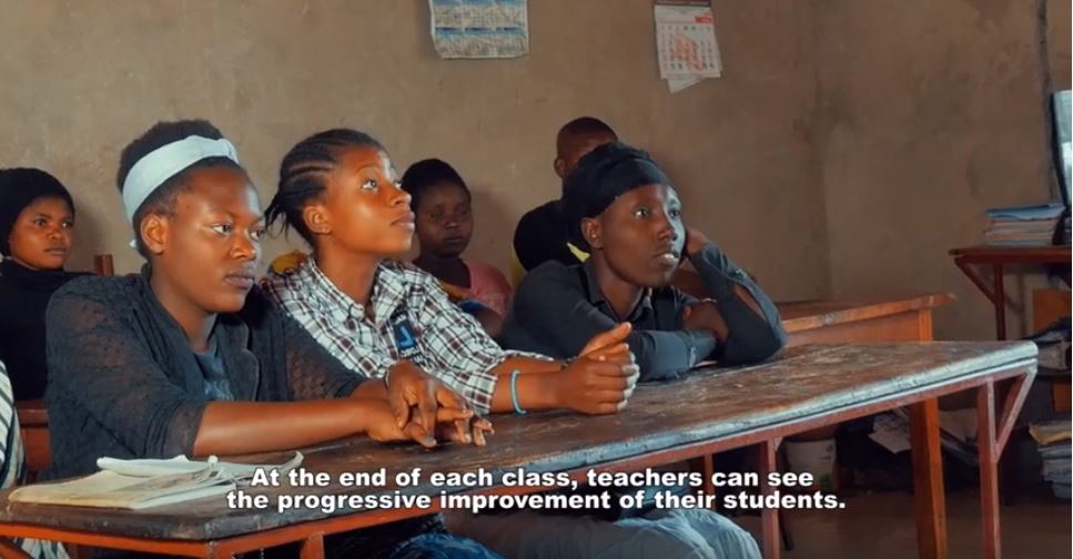 Image of several students sitting at school desks. Below is a closed caption that reads "At the end of each class, teachers can see the progressive improvement of their students."