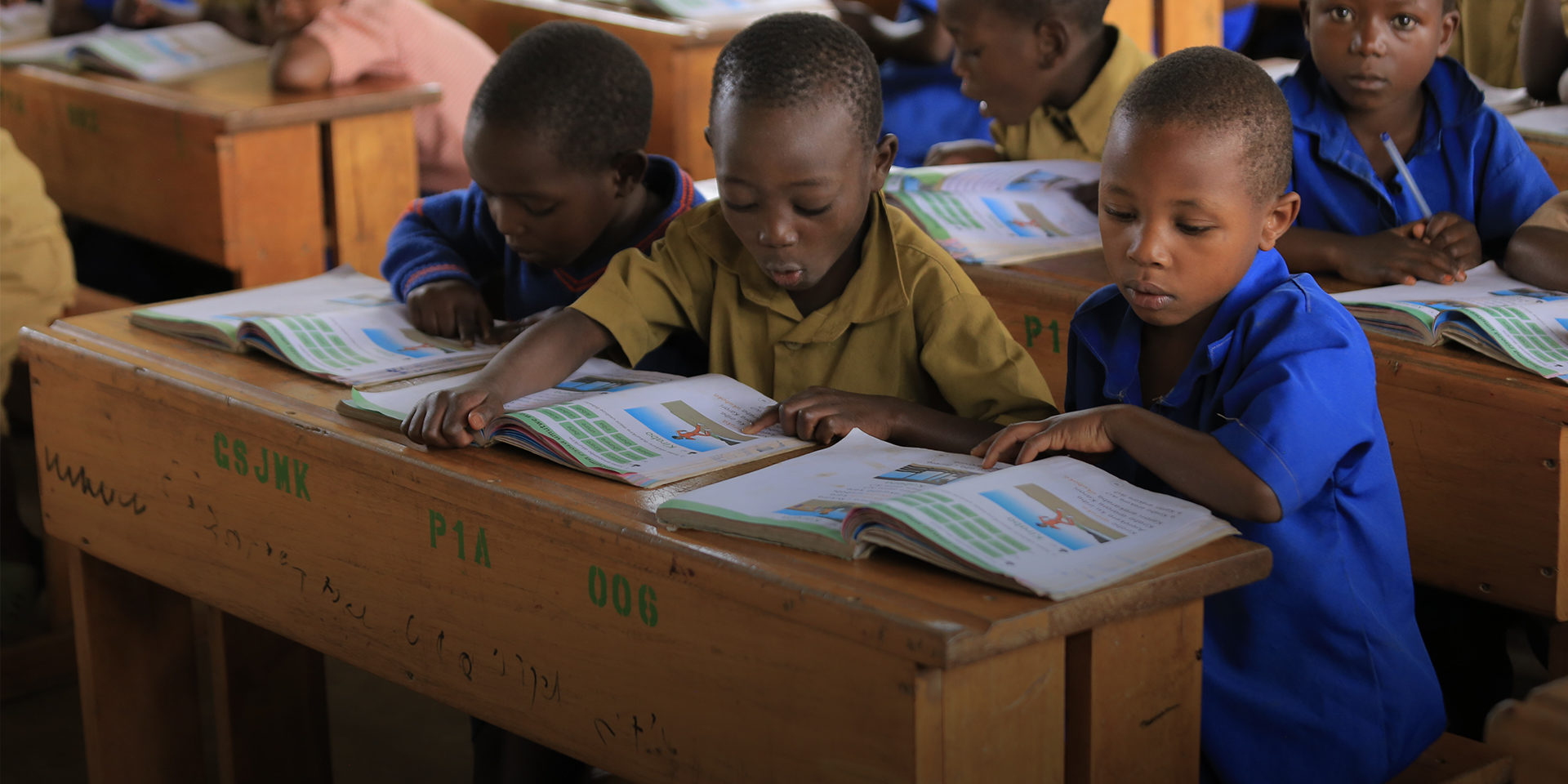 Three children sitting at a school desk and reading from individual books.