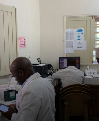 Image of two pharmacists working in a pharmacy as patients wait at windows.