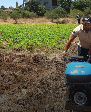 Image of a man operating a motorized fertilization machine as several people in the background look at the field.