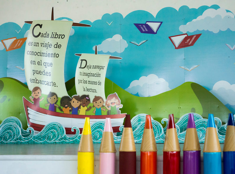 A cartoon mural including a boat filled with children sailing past green mountains. Several books opened to appear like birds are in the sky.