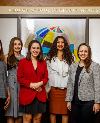 Six professionals posing for a photo in front of a wall that reads "Keough School of Global Affairs."