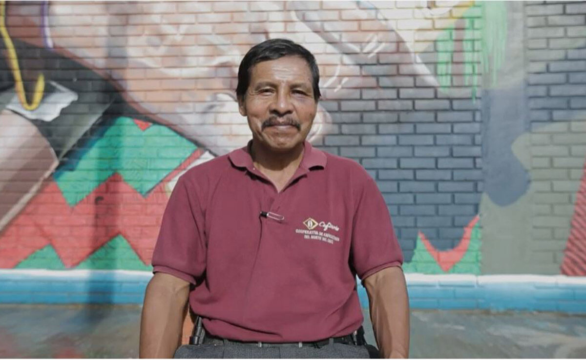 A person sitting and smiling in front of a mural on a brick wall.
