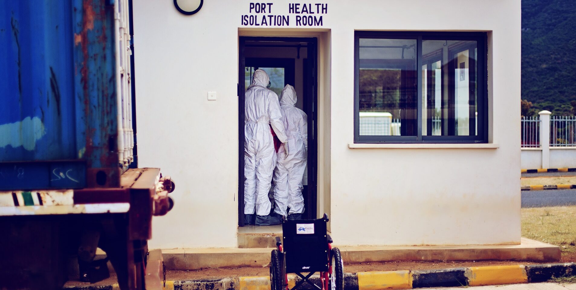 Image of two people in hazmat suits standing inside a doorway with 