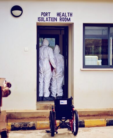 Image of two people in hazmat suits standing inside a doorway with "Port Health Isolation Room" written above.