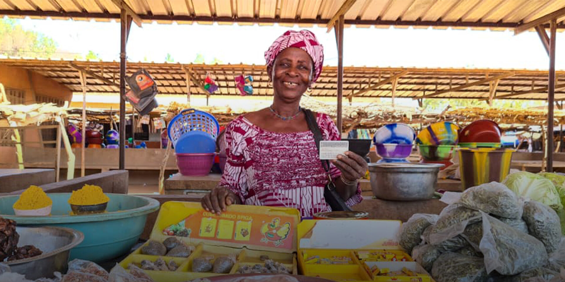 A woman minding a stall selling herbs and spices. She is smiling and holding up a card.