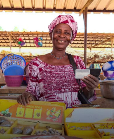 A woman minding a stall selling herbs and spices. She is smiling and holding up a card.