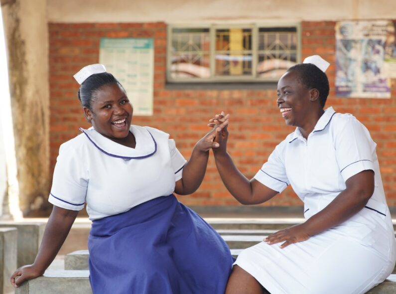 Two healthcare workers sitting outside and smiling as they give each other a high five.