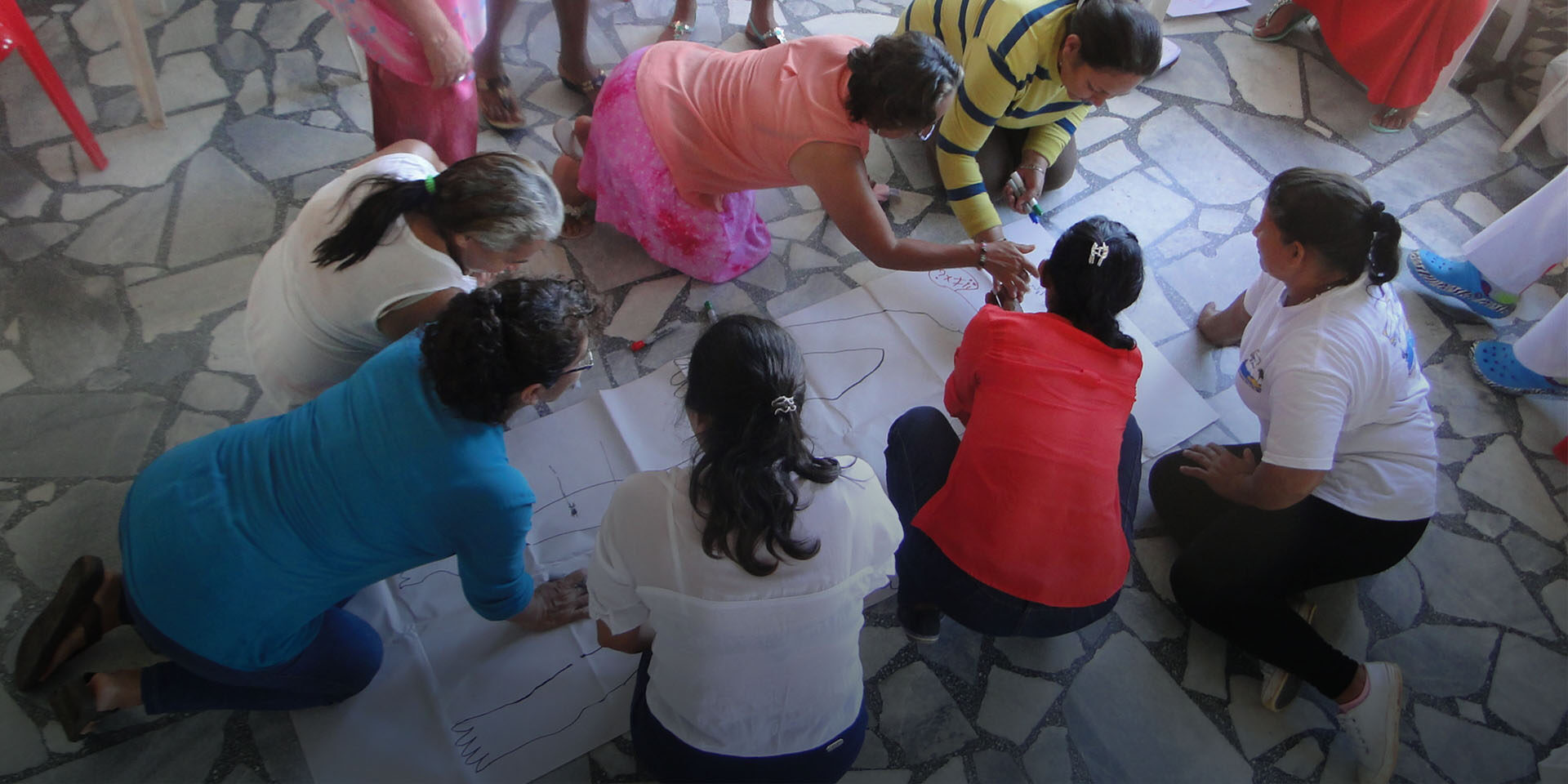 Image of several people kneeling around a drawing of a person and working together to solve an educational exercise.