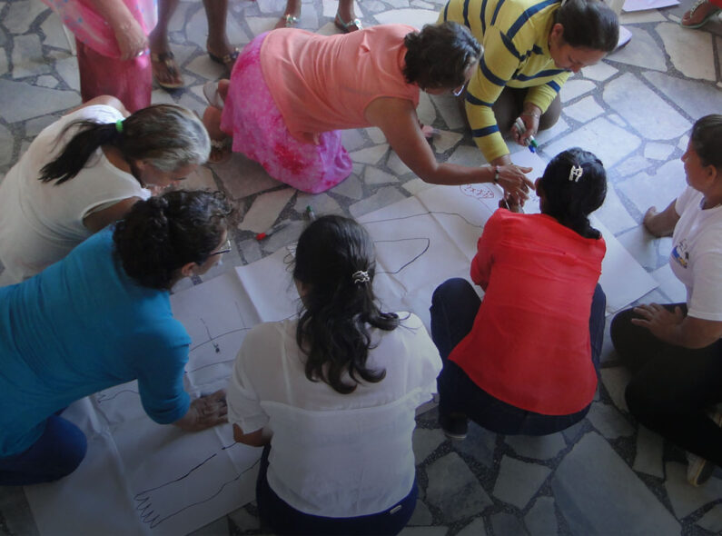 Image of several people kneeling around a drawing of a person and working together to solve an educational exercise.