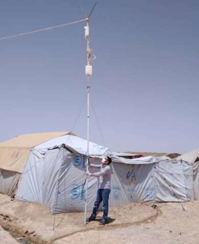 A man holding onto a large telecom pole outside of a tent city.