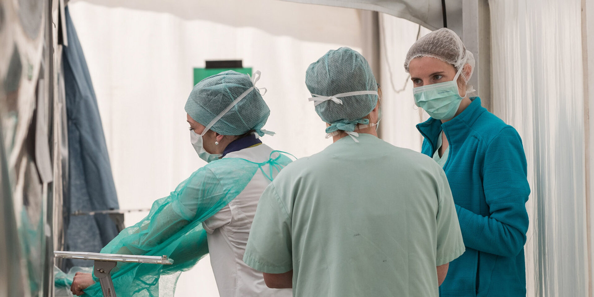 Three healthcare workers wearing scrubs and protective masks standing outside of an operating room.